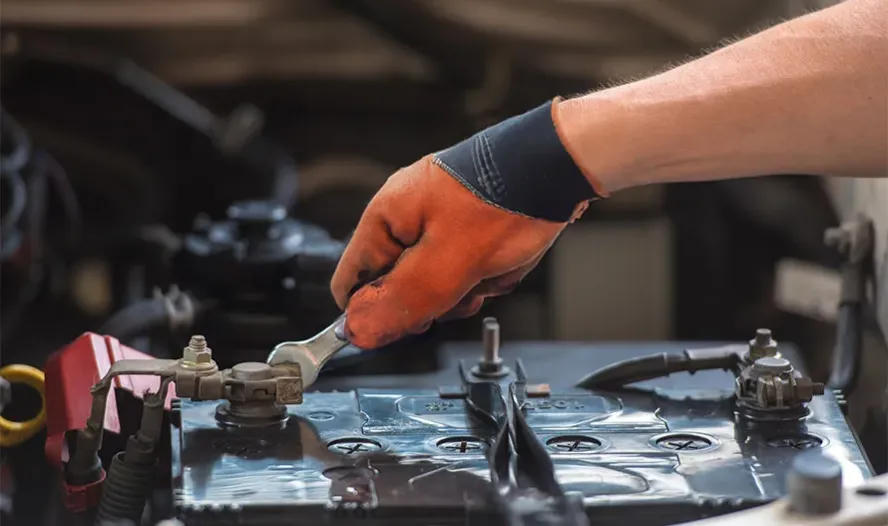Gloved hand loosening a battery terminal with a wrench